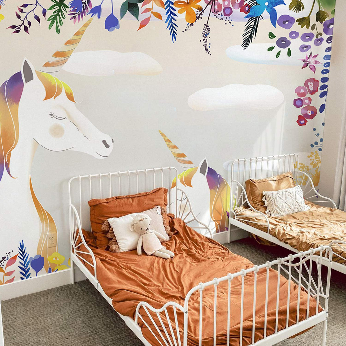 Enchanting Unicorn Mural Wallpaper features vibrant florals, white metal beds, and plush bear in children's bedroom.