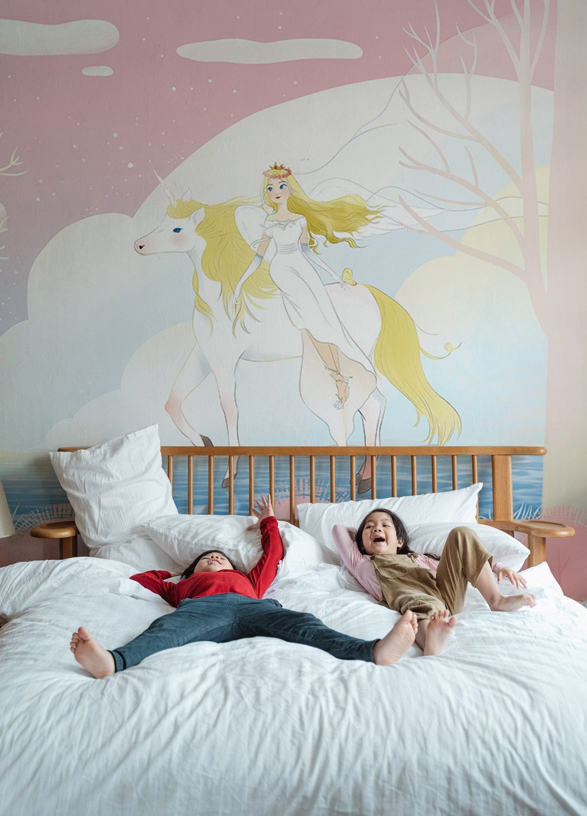 Children's bedroom with pastel unicorn mural wallpaper, wooden bed, white bedding, playful fantasy decor.