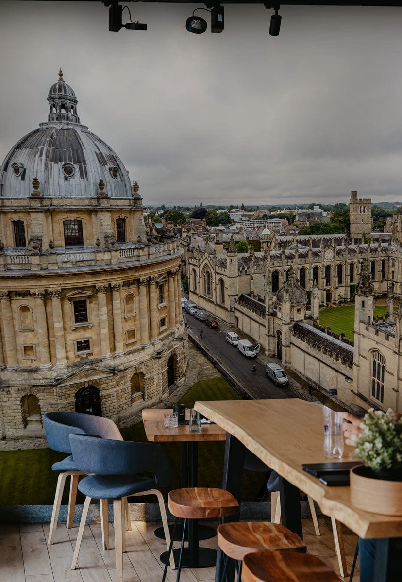 Classic British University Architecture Mural, elegant grey tones, wooden dining table, navy chairs, light flooring.