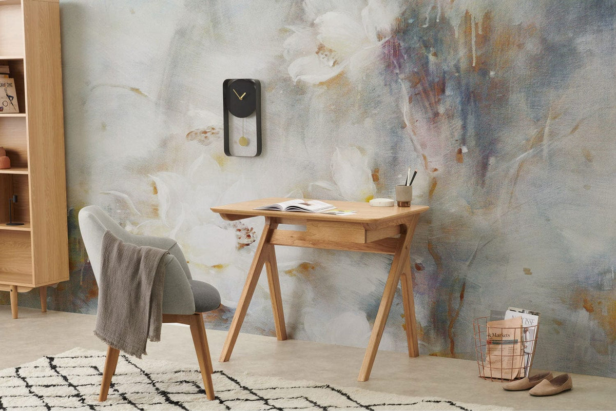Ethereal floral mural wallpaper with soft pastels, light wood furniture, and a grey upholstered chair.