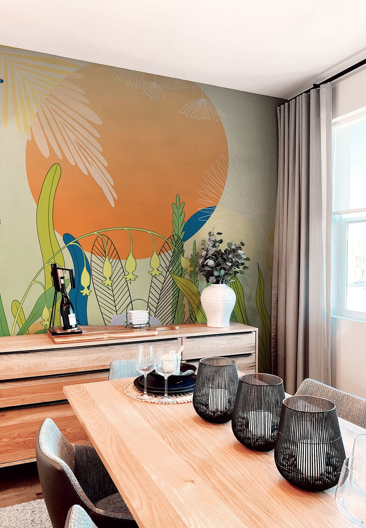 Dining room with Tropical Sunset Botanical Mural Wallpaper, colourful nature design, wooden table, grey chairs.