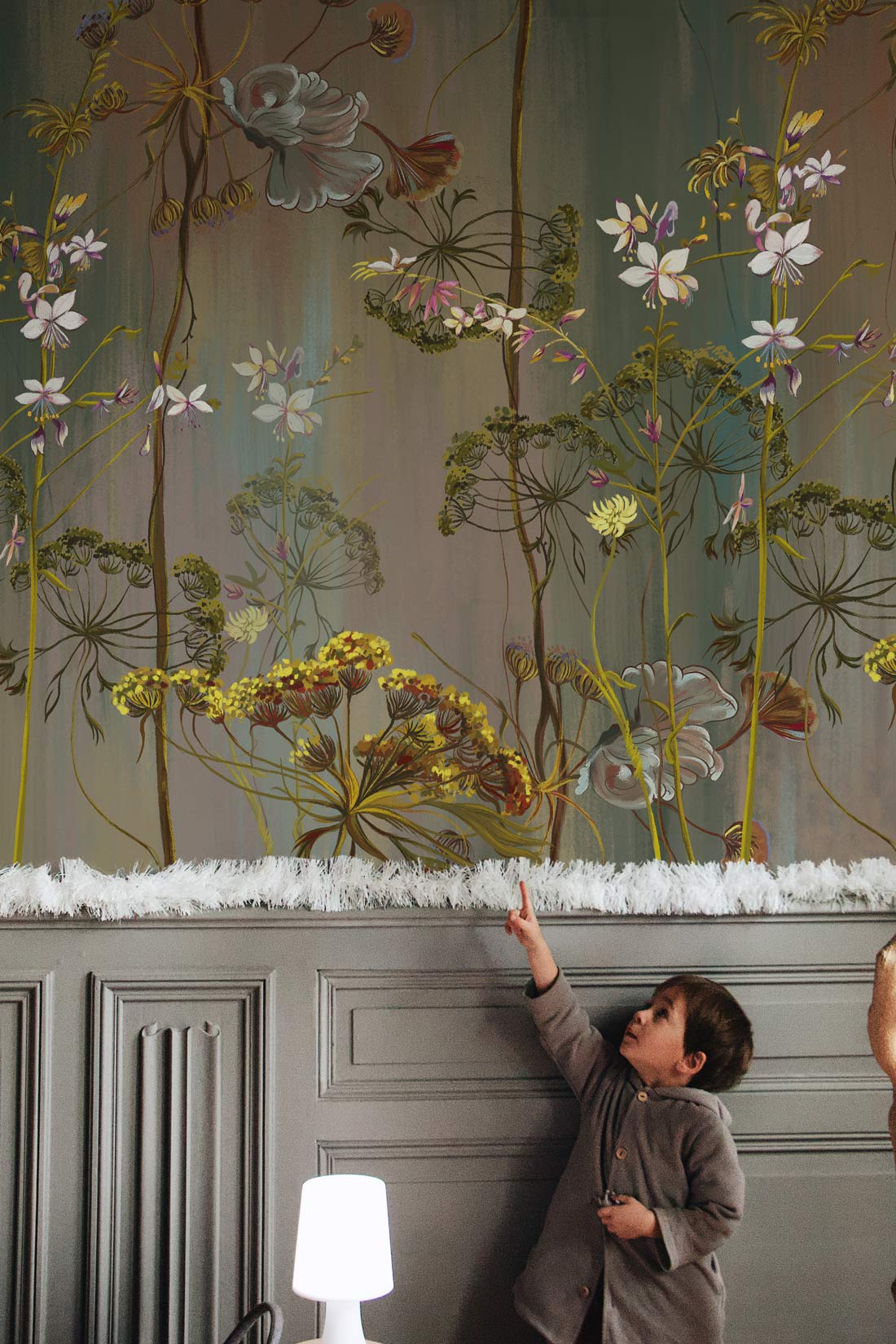 Vintage botanical floral mural wallpaper in rich green tones, elegant wood panelling, child pointing in room.