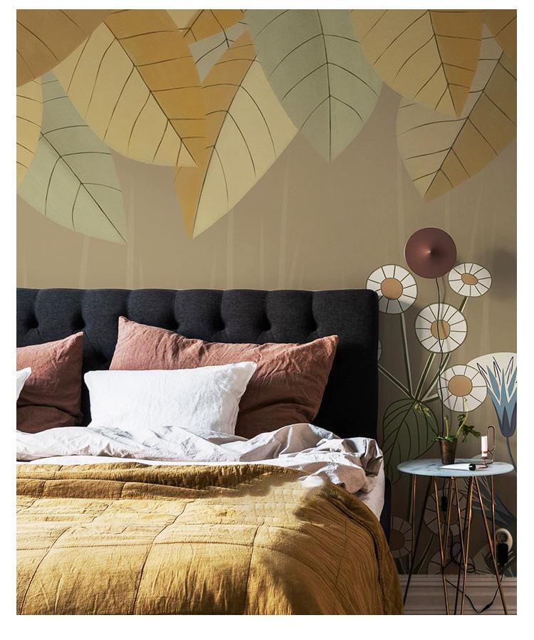 Botanical Harmony mural wallpaper with earthy leaves behind modern black headboard and mustard bedding in bedroom.