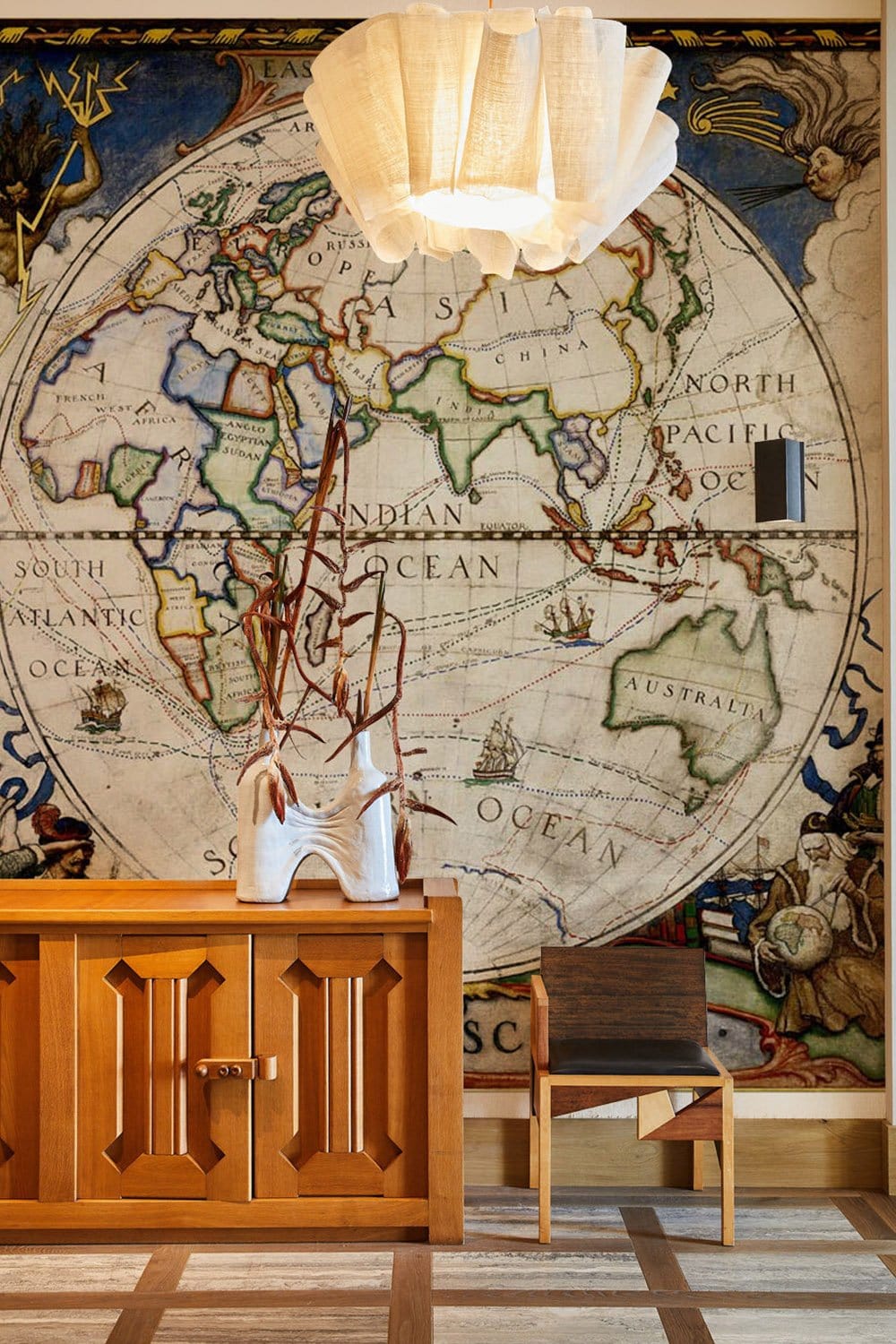 Vintage World Map Mural Wallpaper, wooden cabinet, modern chair, pendant lamp, and striped flooring.
