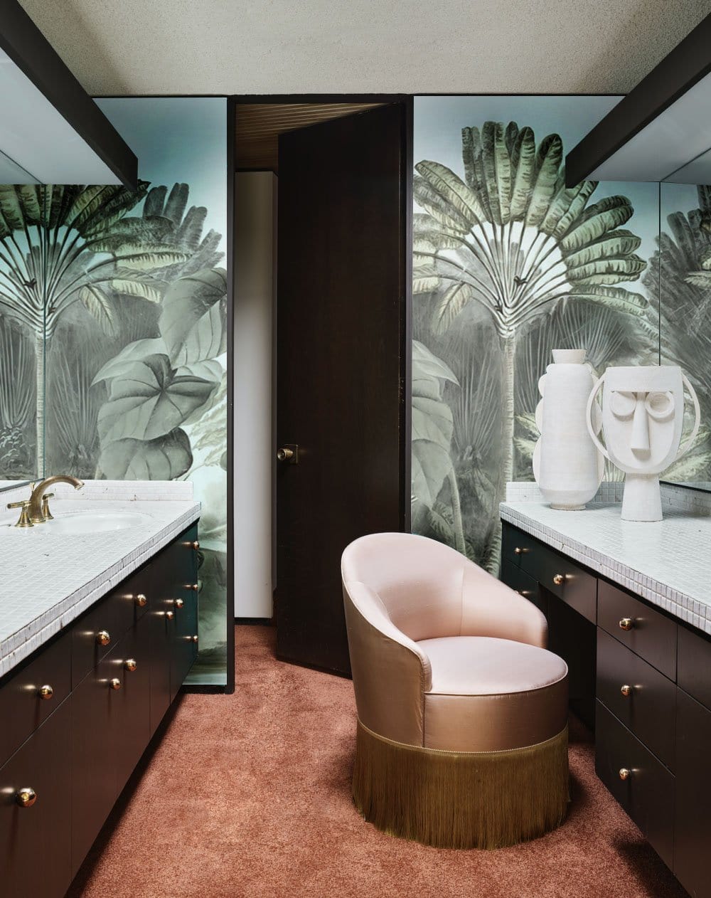 Vintage tropical botanical wallpaper, soft green-grey, bathroom with pink velvet chair, dark cabinets, brown carpet.