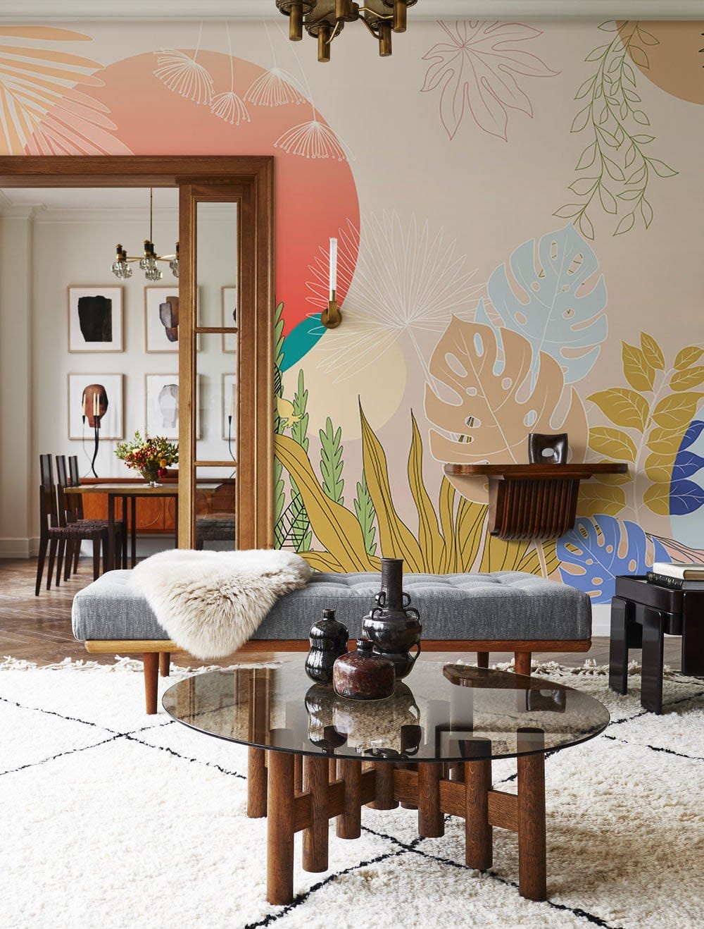 Vibrant tropical mural wallpaper in elegant room with grey bench, plush rug, glass table.