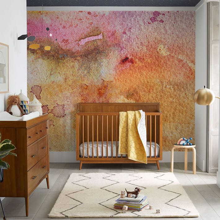Abstract Watercolour Sunset Bliss Wall Mural with wooden cot, dresser, beige rug in nursery room.