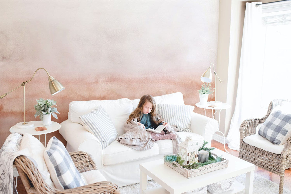 Elegant watercolour blush gradient wallpaper in cosy living room with white sofa and wicker armchairs.