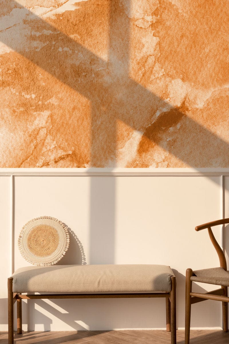 Earthy watercolour textured orange mural wallpaper with beige bench, wooden chair, and white panelled wall.