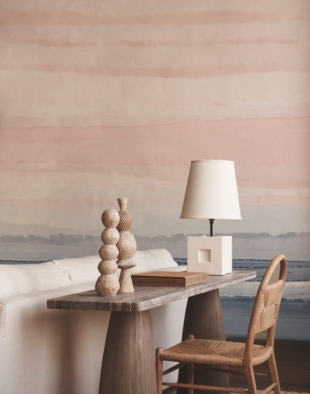 Pastel watercolour mural wall, light sofa, rustic wood desk, woven chair, soft lighting, cosy space.