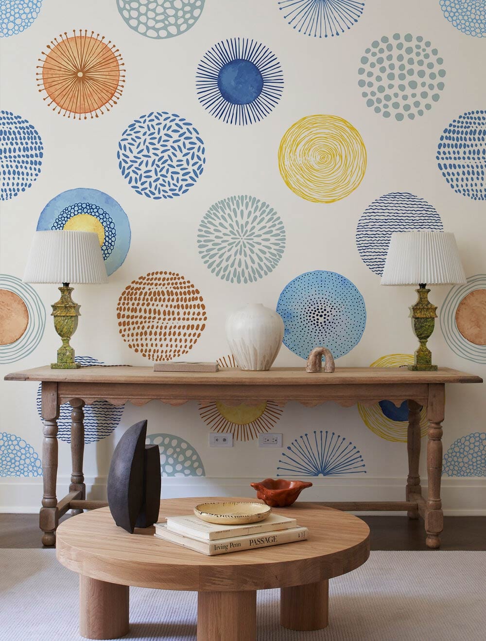 Blue, yellow, orange geometric circle wallpaper with wooden table, lamps, round coffee table, and neutral flooring.