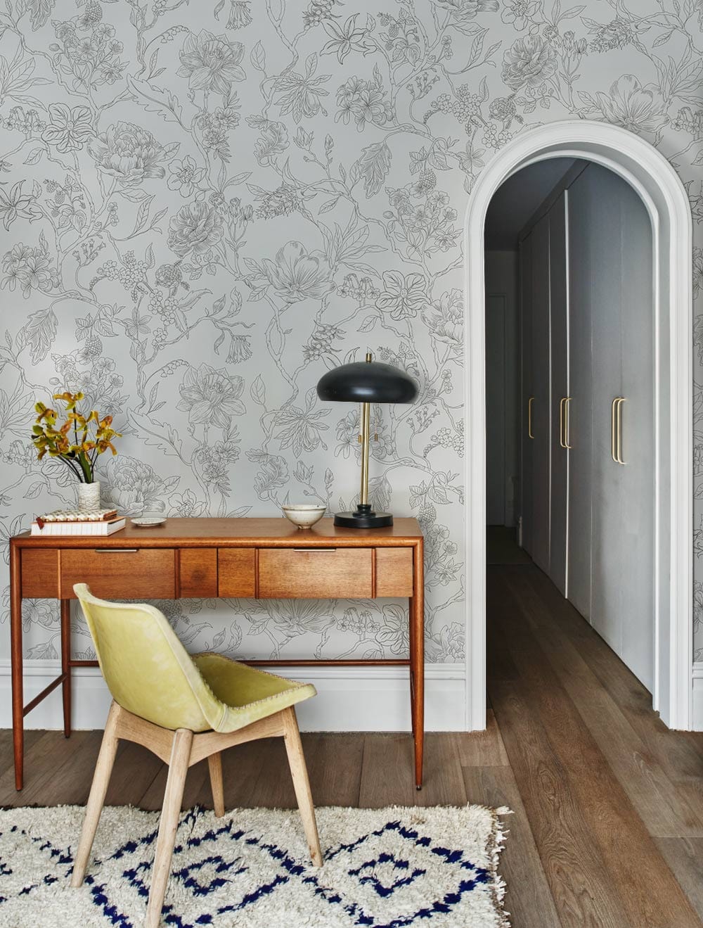 Elegant grey botanical wallpaper in modern study with wooden desk, yellow chair, and patterned rug.