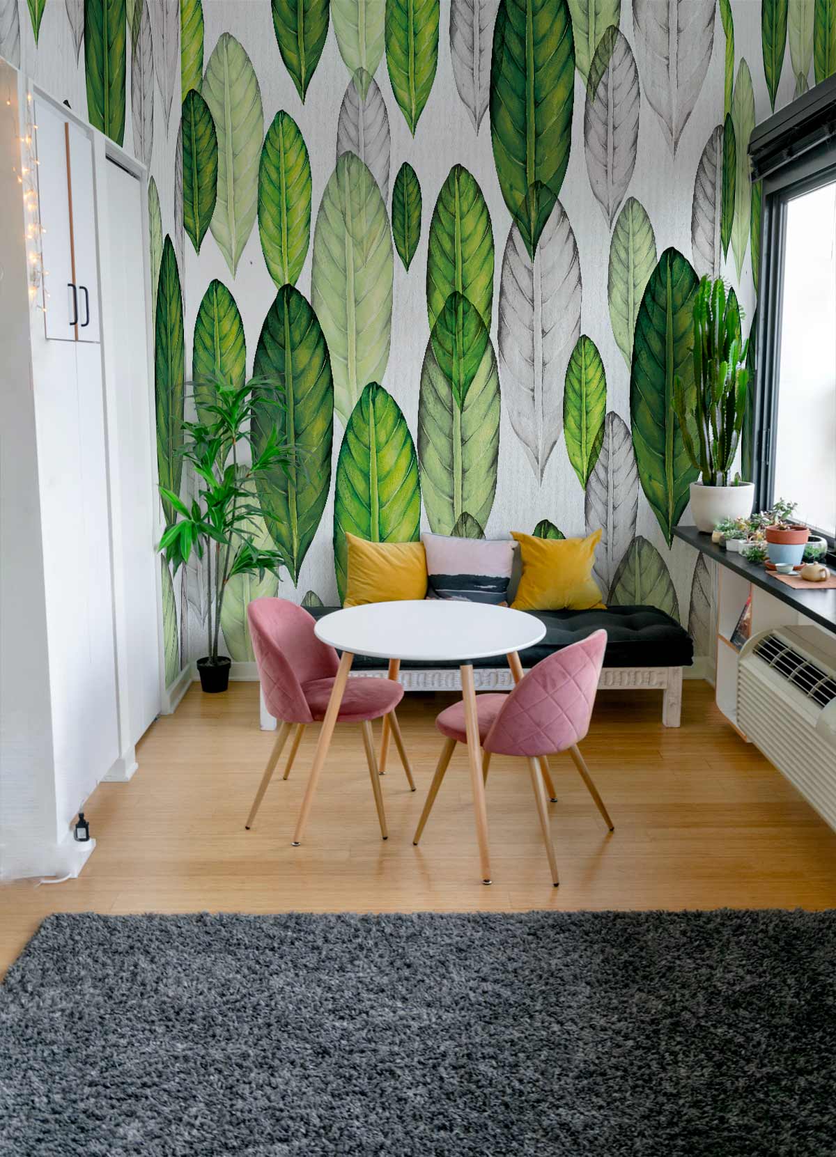 Green botanical wallpaper with leaf pattern in cosy room, pink chairs, grey rug, wooden floor.