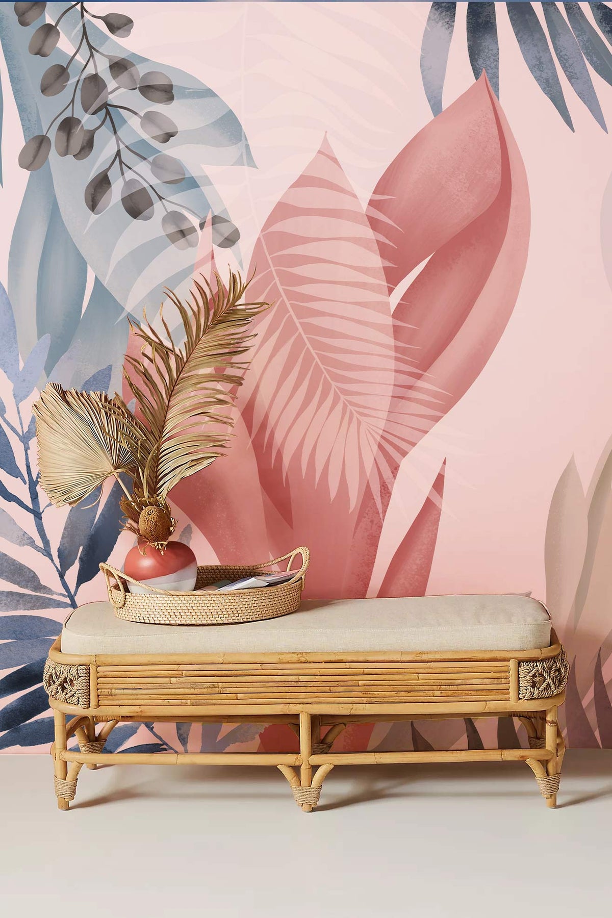 Elegant pastel tropical leaves mural wallpaper with bamboo bench, in soft pink and blue hues.