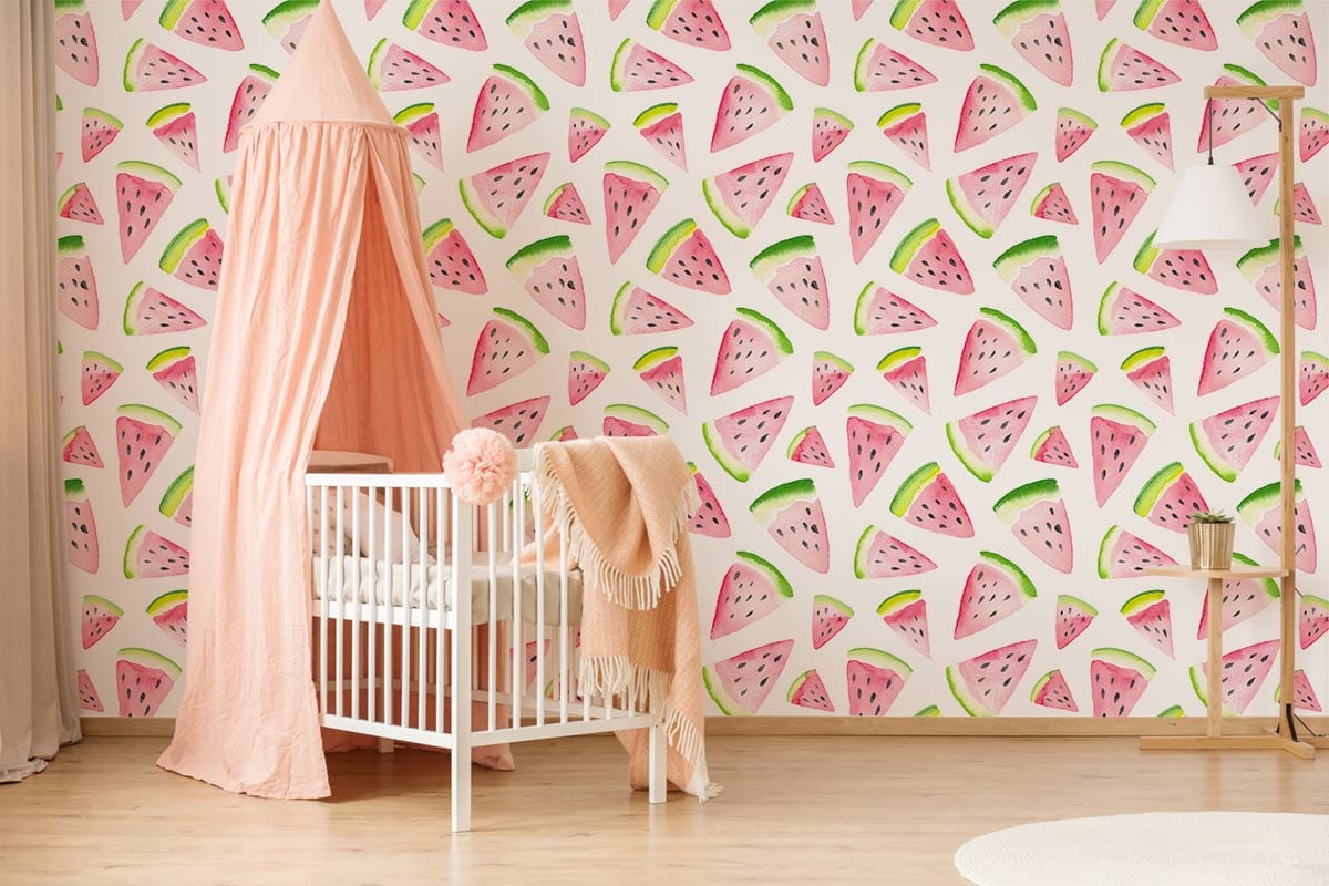 Pink and green watermelon wallpaper in nursery, featuring white crib, peach canopy, wooden flooring.