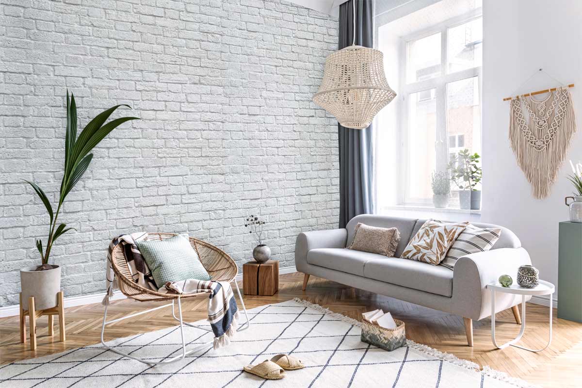 Rustic white brick wallpaper in living room with grey sofa, wicker chair, wooden flooring, and macramé decor.