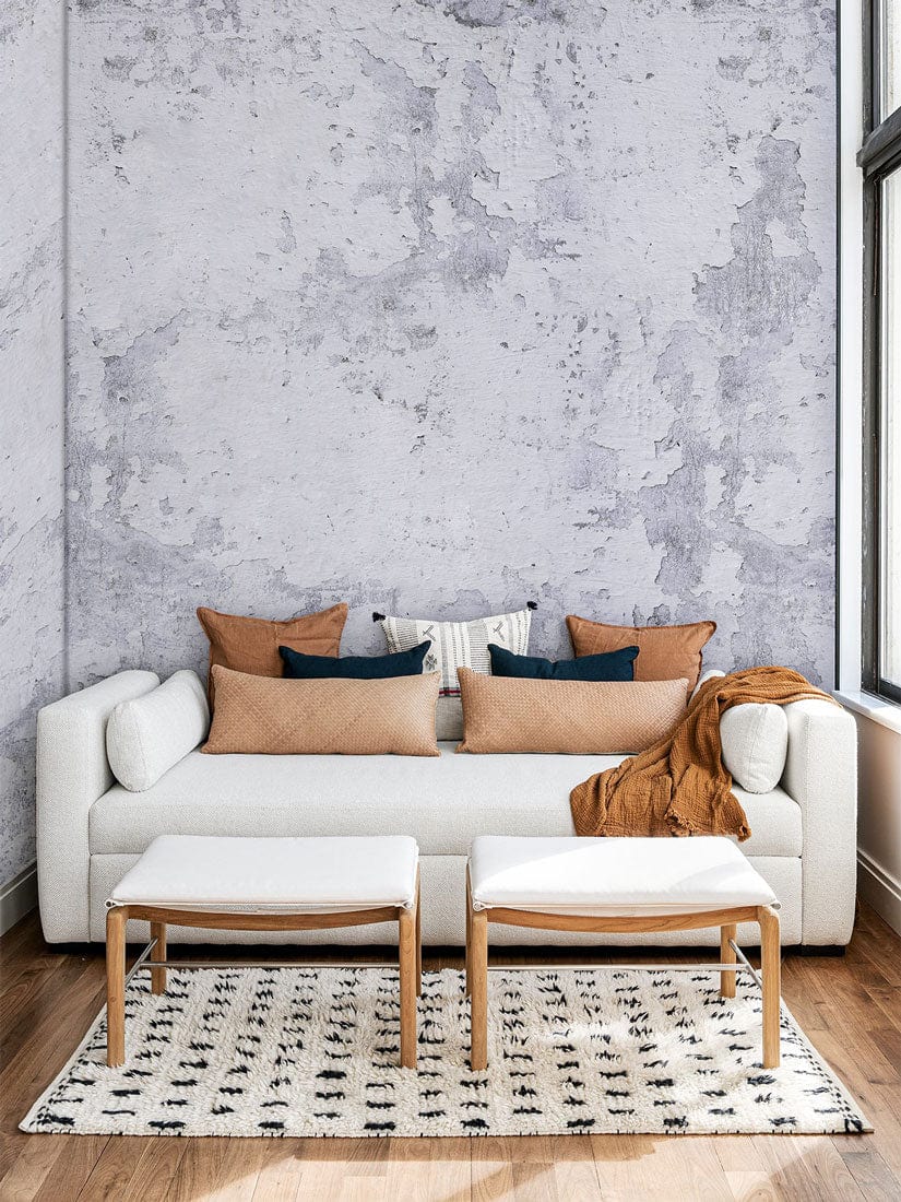 Vintage industrial grey concrete wallpaper complements modern beige sofa, wooden flooring, geometric rug, cushions.