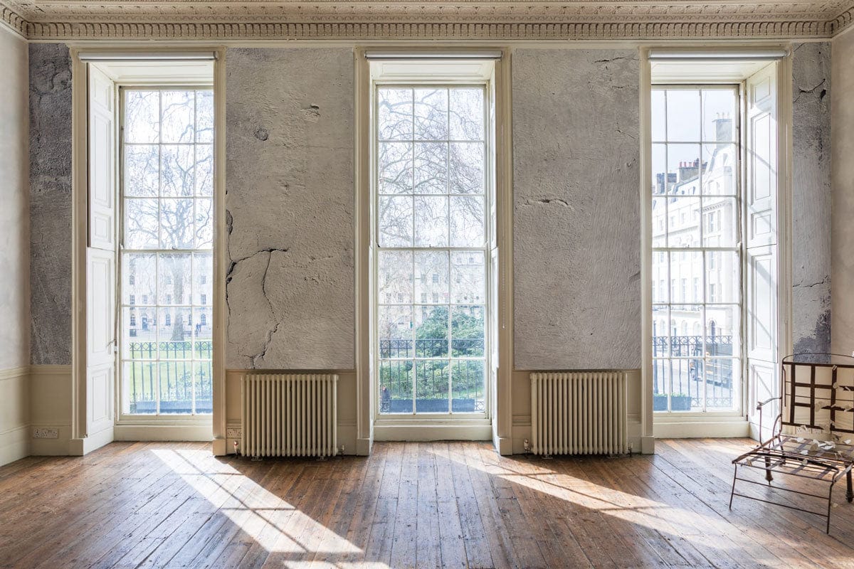 Rustic grey textured wallpaper in bright room with large windows, wooden flooring, and metal chair.