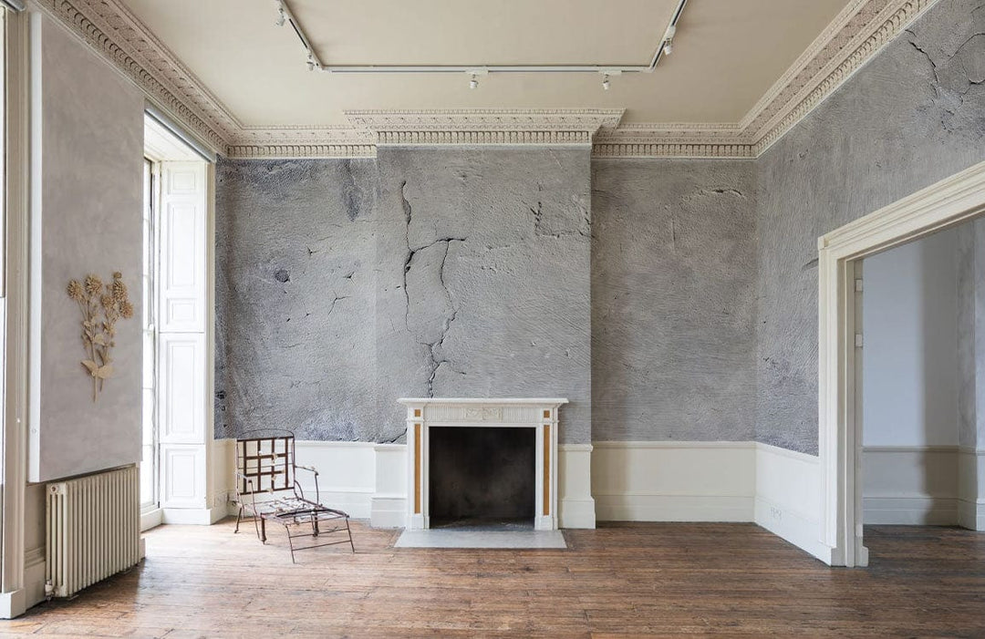 Rustic grey concrete effect mural wallpaper in elegant room with wooden flooring and classic fireplace.