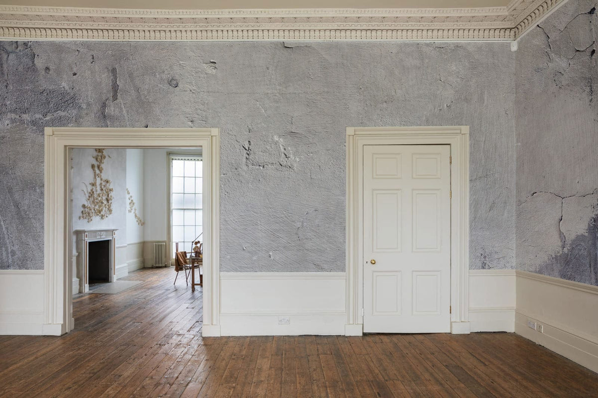Rustic grey concrete effect mural wallpaper in elegant room with wooden flooring and white trim.