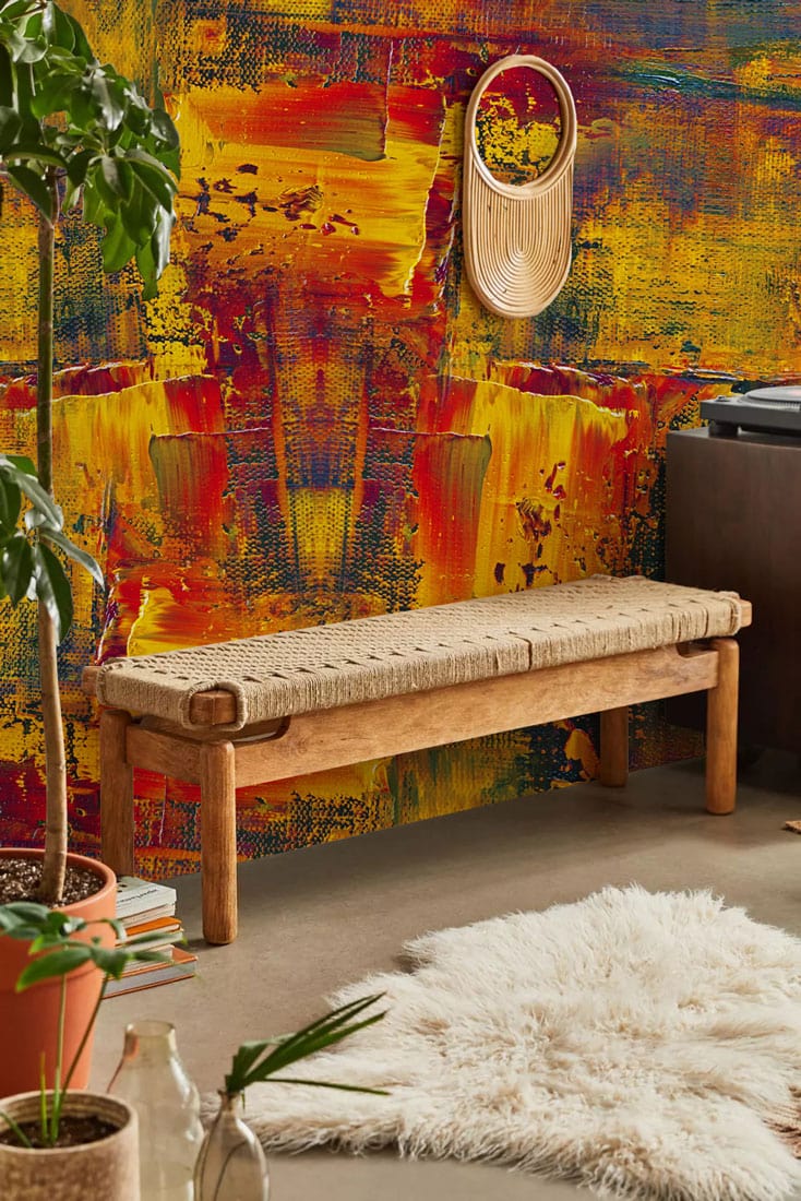 Vibrant mural wallpaper with red and gold hues, rustic bench, modern decor in living room.