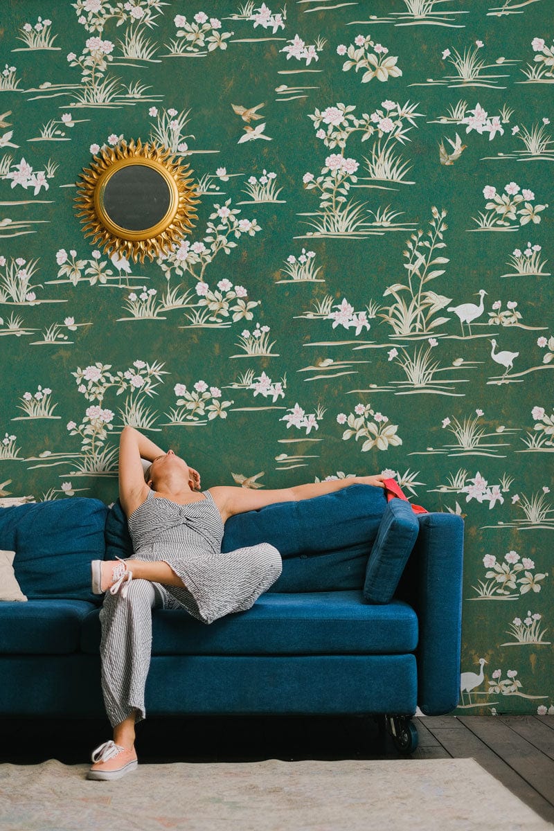 Vintage green floral wallpaper with nature-inspired pattern, blue modern sofa, gold mirror, wooden flooring.