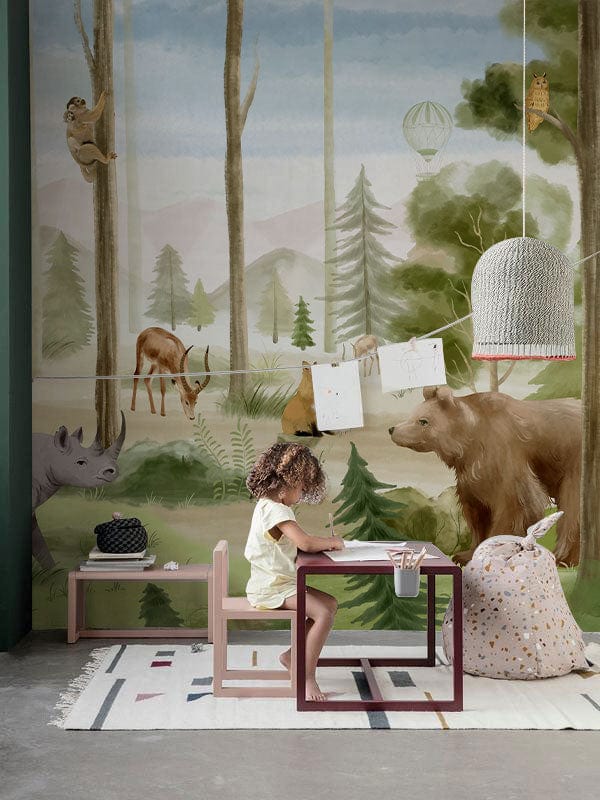 Child's room with Scenic Forest Adventure Animal Mural Wallpaper, colourful rug, cosy seat, and table.