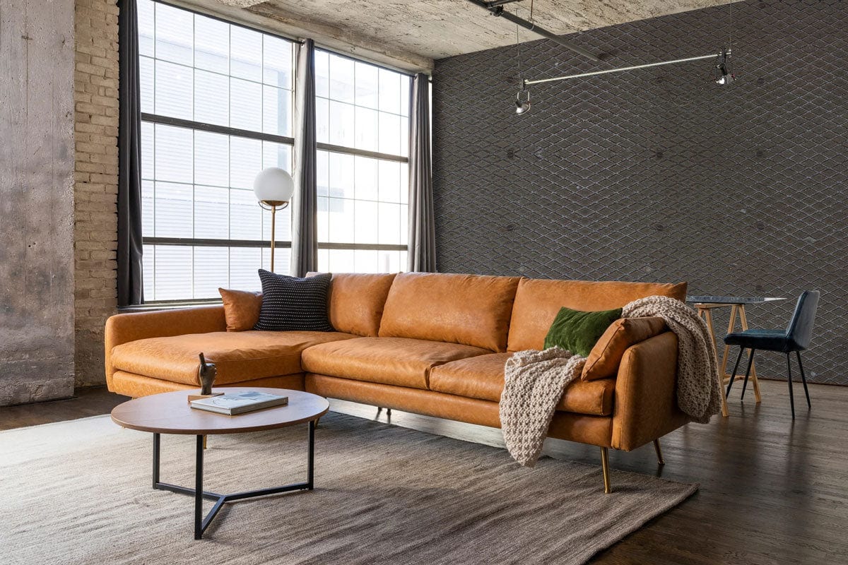 Modern living room with brown leather sectional sofa, industrial grey wall, wooden flooring, and round table.