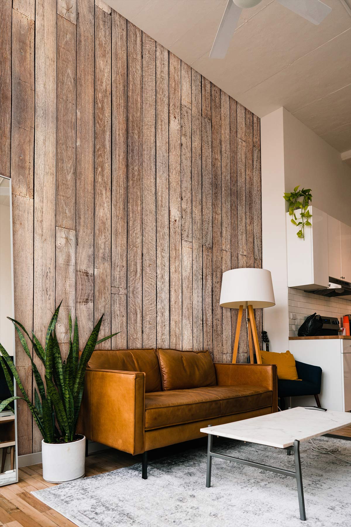 Rustic wooden plank wallpaper accenting living room with brown leather sofa, white lamp, modern decor.