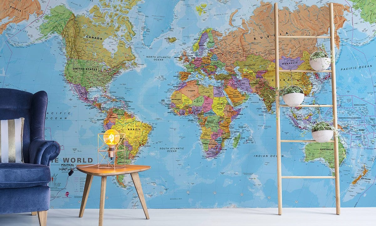 Vibrant World Map mural wallpaper in modern room, blue armchair, light wood ladder and small table.