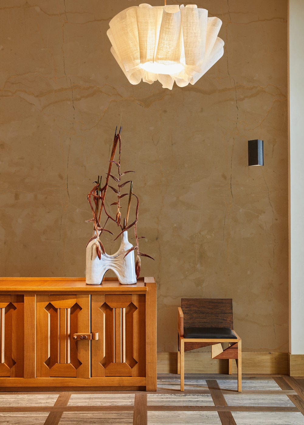 Elegant beige marble effect wallpaper accentuates wooden sideboard, minimalistic chair, and pendant light.