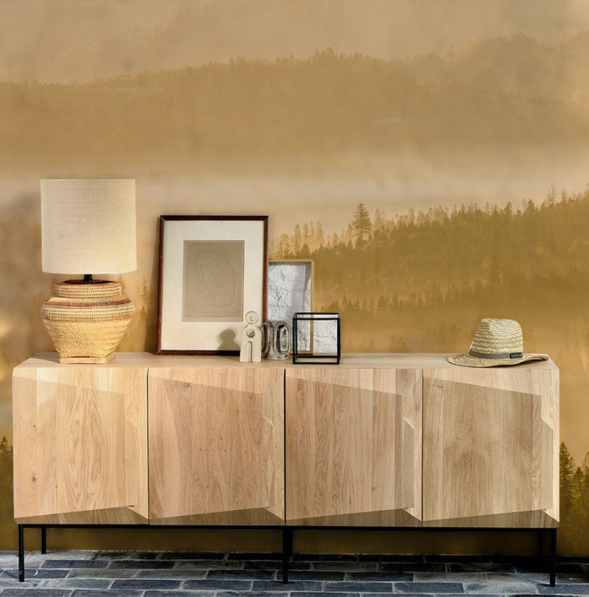 Golden Misty Forest Mural Wallpaper with natural wood sideboard, lamp, rustic decor; stone flooring.