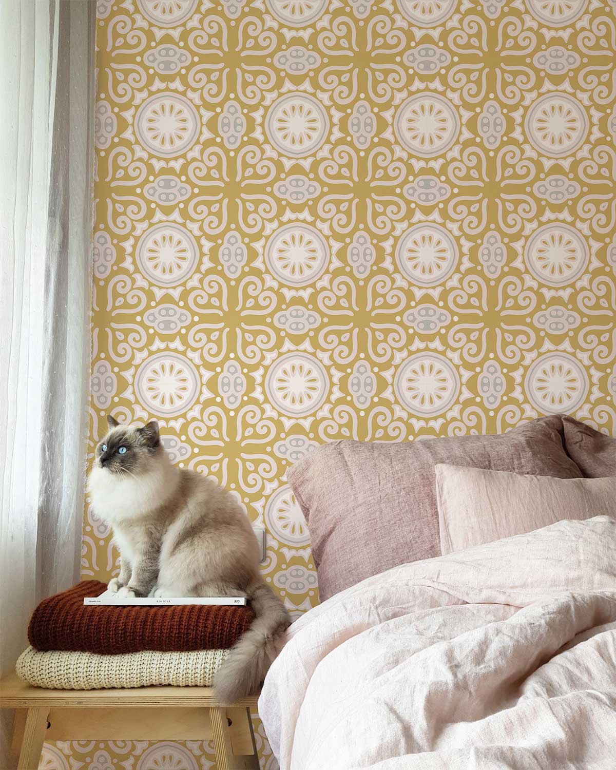 Vintage gold ornate wallpaper in bedroom with beige bedding and fluffy cat on stool. Victorian style.