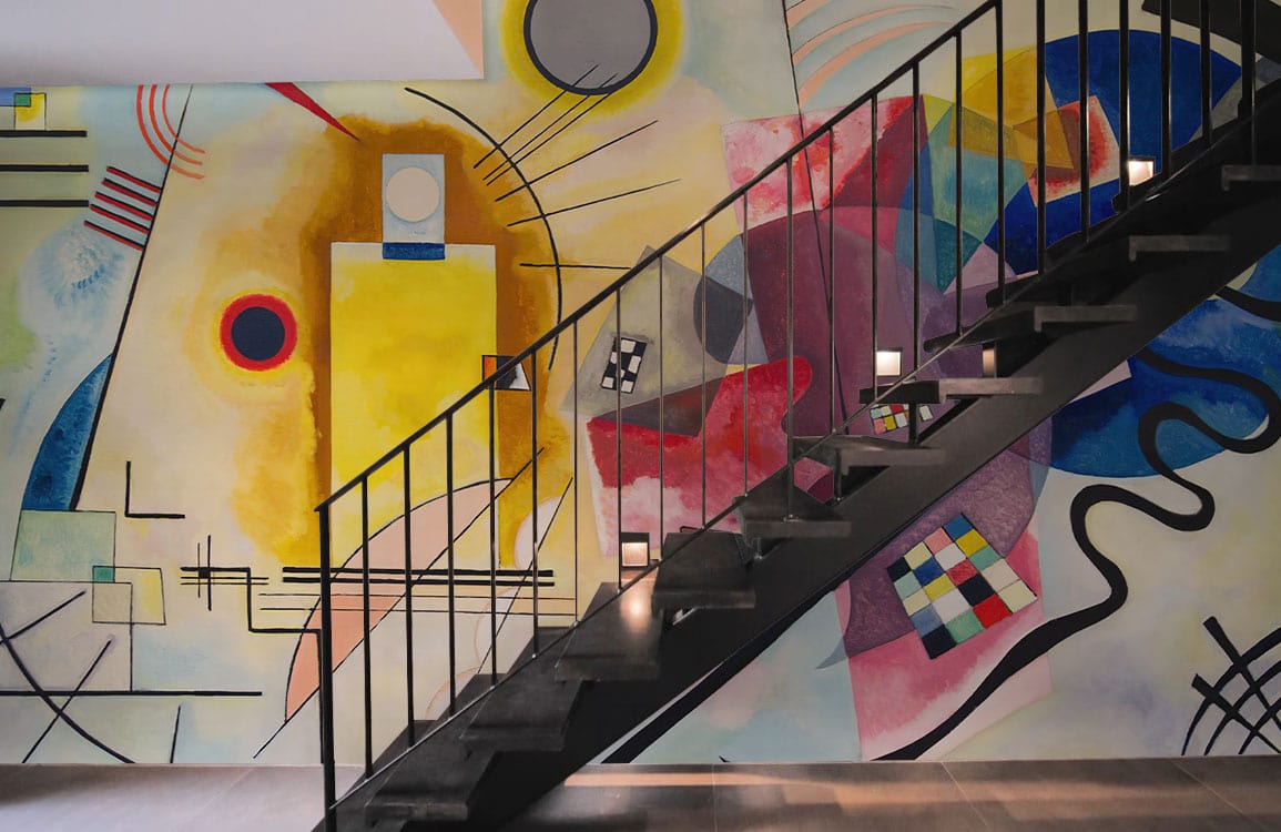 Vibrant Art Deco mural with geometric shapes featuring staircase; stylish modern interior with muted flooring.