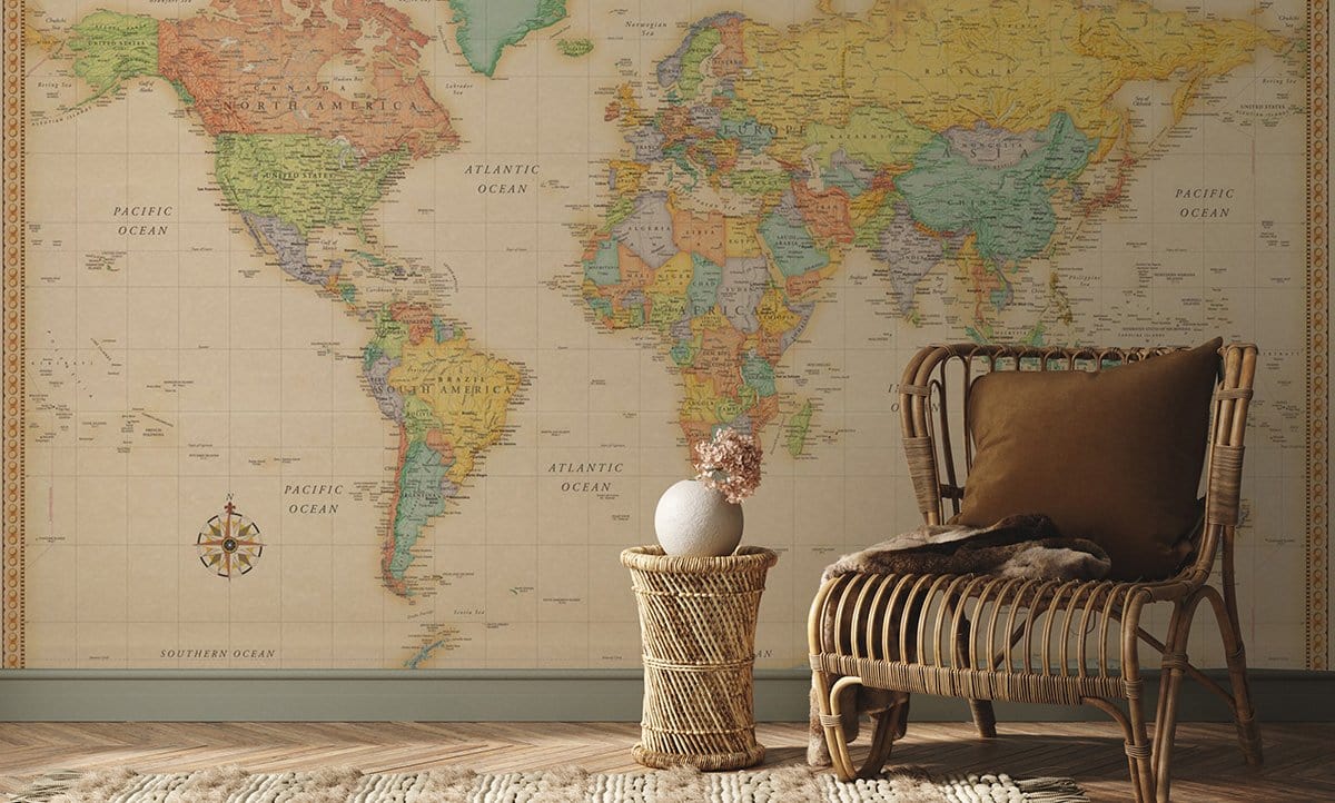 Vintage world map mural wallpaper in antique earth tones with wicker chair on wooden floor.